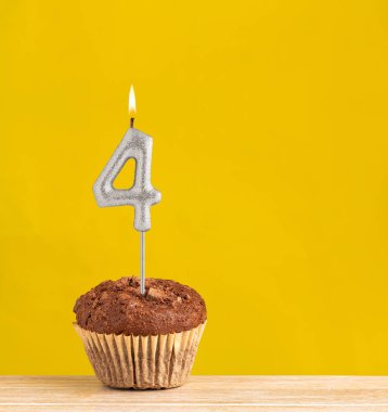 Chocolate cupcake with number 4 candle - Birthday on a yellow background.