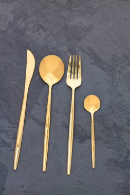 Zarif altın çatal bıçak takımı. Çatal, bıçak ve kaşıklar karanlık bir taş arka planda.