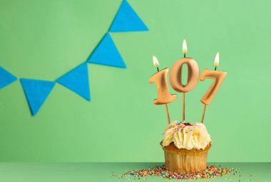 107 numaralı mumlu doğum günü kartı mavi flama ile yeşil arka planda kek..