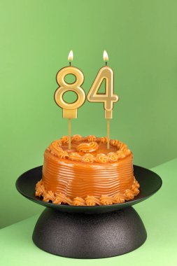 Lezzetli pasta, dulce de leche - 84 numaralı doğum günü mumu yeşil arka planda..