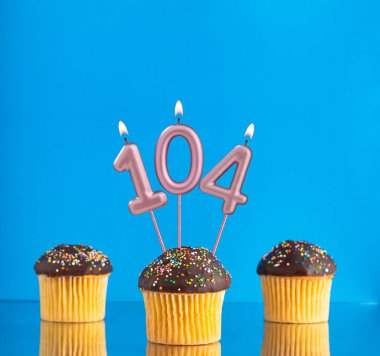 104 numaralı doğum günü mumuyla mavi arka planda üç kek..