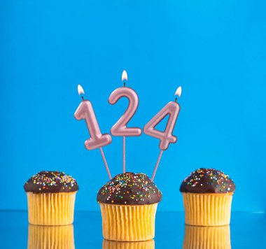 124 numaralı doğum günü mumuyla mavi arka planda üç kek.