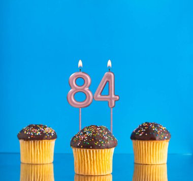 84 numarayla doğum günü mumu - Mavi arka planda üç kek.