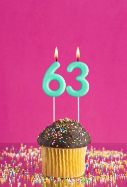 63 numaralı mumlu doğum günü keki fuşya arka planında kutlama kartı.