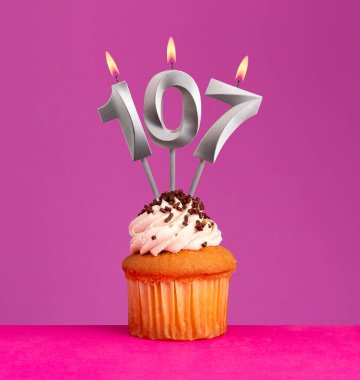 107 numaralı doğum günü mumu ve menekşe arka planında kek.