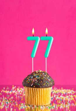 77 numaralı mumlu doğum günü keki fuşya arka planında kutlama kartı