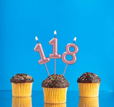 118 numaralı doğum günü mumuyla mavi arka planda üç kek.