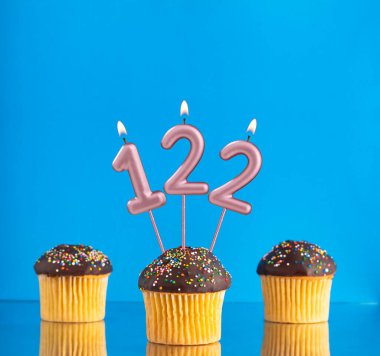122 numaralı doğum günü mumuyla mavi arka planda üç kek.