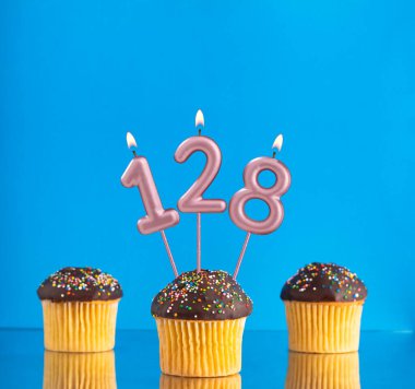 128 numaralı doğum günü mumuyla mavi arka planda üç kek.
