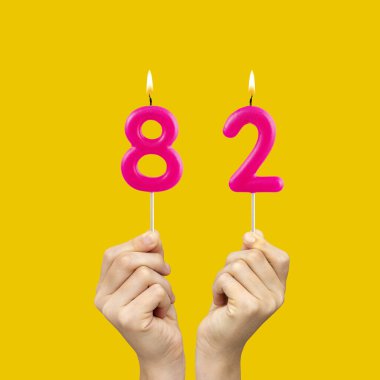82 numaralı doğum günü mumlarını tutan eller - Sarı arka plan