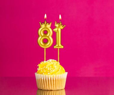 Sarı doğum günü pastası, üzerinde 81 numara mum pembe arka planda doğum günü kartı.
