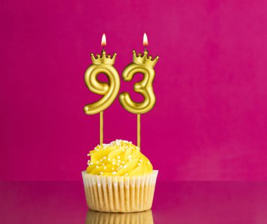 Pembe arka planda 93 numaralı mumlu sarı doğum günü pastası.