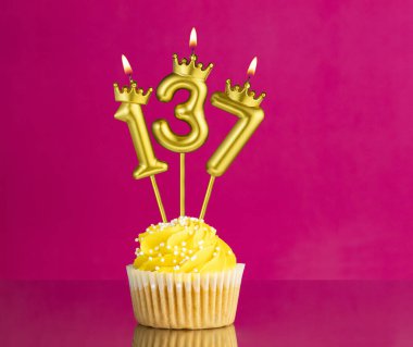 Pembe arka planda 137 numaralı mumlu sarı doğum günü pastası.