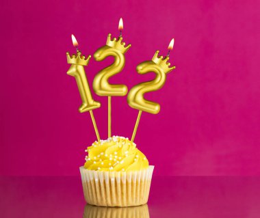 122 numaralı mumla doğum günü kutlaması. Pembe arka planda sarı kek.