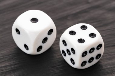 Siyah noktalı iki beyaz zar karanlık bir masada.