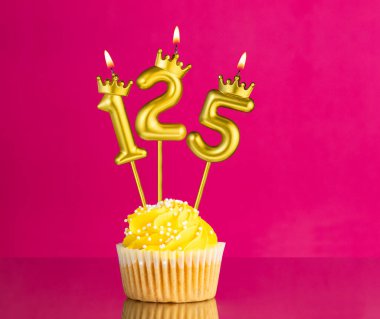 Sarı doğum günü pastası, üzerinde 125 numara mum pembe arka planda doğum günü kartı.