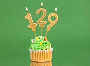 129 numaralı doğum günü mumu. Yeşil arka planda kek.
