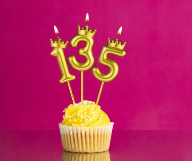 Sarı doğum günü pastası, üzerinde 135 numara mum pembe arka planda doğum günü kartı.
