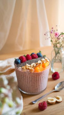 Fresh smoothie bowl with berries, nuts and chia seeds on wooden table. The bright colors of fruits and berries combined with green vegetation in the background create an atmosphere of clipart