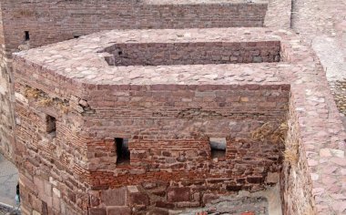 Yüksek açılı, yakından bakınca eski kale duvarlarının yıpranmış dokusunu ortaya çıkarıyor. Kırmızımsı kahverengi tuğlalar ve taşlar titizlikle düzenlenmiştir. Geçmiş zamanların zanaatkarlığını sergilerler. Küçük, dikdörtgen açıklıklar, muhtemelen ok yarıkları, noktalama işaretleri.