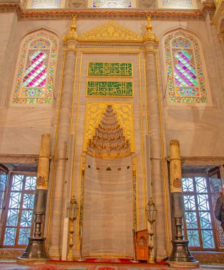 Çarpıcı bir İstanbul camii içindeki karışık mihrab 'ı gösteren ayrıntılı bir fotoğraf. Görüntüde süslü altın detaylar, canlı vitraylı pencereler ve zarif mermer mimari yer alıyor. İslam sanatı ve mimarisi ile ilgili projeler için ideal