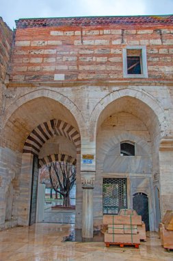 Antik kemer ve tuğla, tarihi İstanbul binasındaki sakin bir avlu çerçevesi. Sahne, bulutlu bir gökyüzü altında Osmanlı mimarisinin karmaşık detaylarını gözler önüne seriyor..