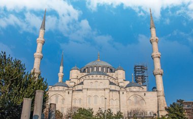 İstanbul, Türkiye 'deki Sultan Ahmed Camii' nin (Mavi Cami) görkemli manzarası. Görüntü caminin etkileyici mimarisini gözler önüne seriyor. Yüksek minareleri, büyük merkezi kubbesi ve parlak mavi gökyüzüne karşı detaylı bir cephe. Surroun.