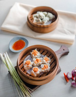 Top view traditional chinese steamed dumplings Dimsum in bamboo steamer on wooden table with chopsticks, sauce, chili and vegetable as decorations