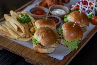 Well served four mini burgers with fries and salad on wooden black background 