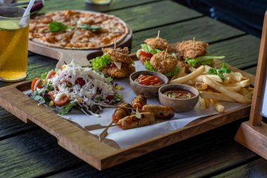 Well served four mini burgers with fries and salad on wooden black background 