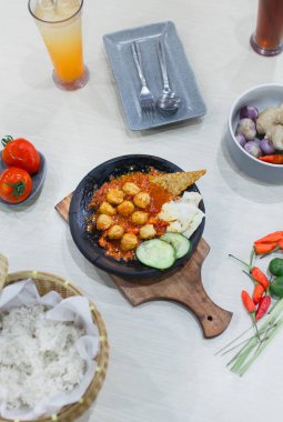 Close up bakso or meatballs with sambal cooked in earthenware plate against wooden background. Served on wooden table with chili, spoon and fork as decoration