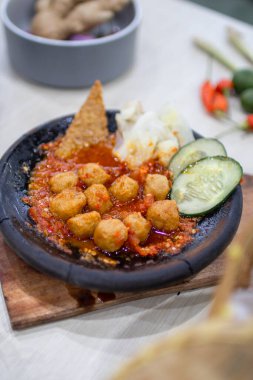 Close up bakso or meatballs with sambal cooked in earthenware plate against wooden background. Served on wooden table with chili, spoon and fork as decoration