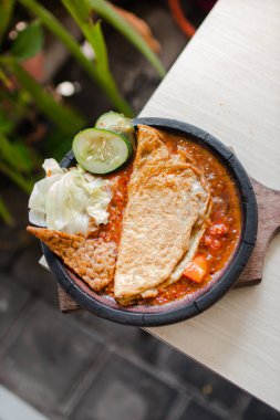 Sambal gami telor dadar or omelete with sambal cooked in earthenware plate against wooden background. Served on wooden table