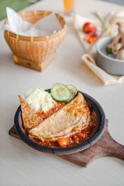Sambal gami telor dadar or omelete with sambal cooked in earthenware plate against wooden background. Served on wooden table