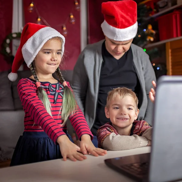 Safe online Christmas celebration. Happy family in Santa red hats celebrating with friends virtually via internet and notebook. Video call. Stay home, distant holiday, lifestyle