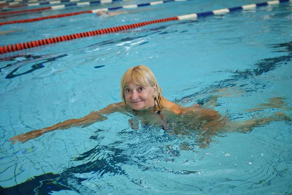 Happy woman 60-65 years old swims at a sports public pool. The concept of slow aging and the fullness of life. Active life at any age