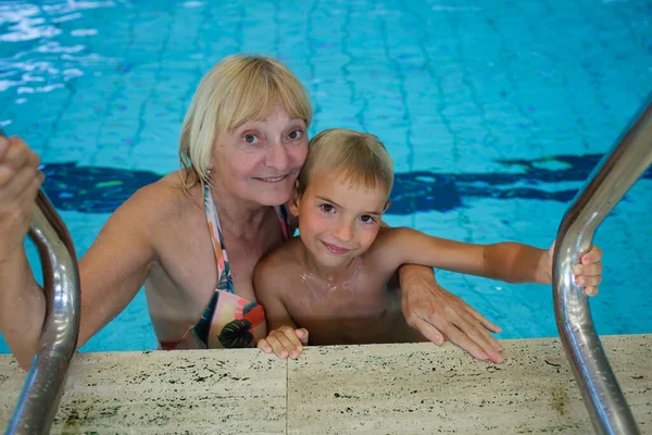 Happy 60 year old woman and grandson swim at public sports pool, symbolizing aging gracefully and strong family bond. Active lifestyle and health emphasized.
