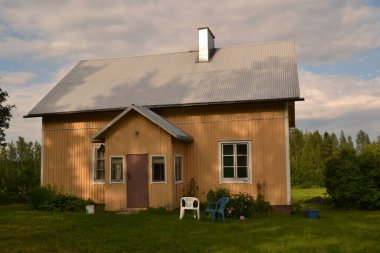 Önünde mavi bir sandalye olan kır evi, yeşil çimenli bir arka bahçe.