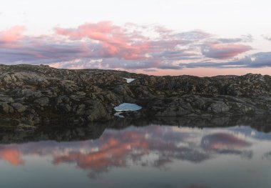 Gün batımında suda yansıması olan dağ gölü, Norveç