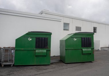 Büyük bir sanayi binasının otoparkında çöp konteynırları.