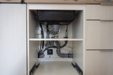 Mutfaktaki lavabonun altında borular olan açık dolap. 