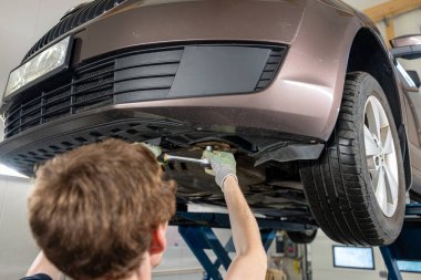 Araba tamircisi kaldırılmış arabanın altında duruyor ve garajda araba tamiri yapıyor.