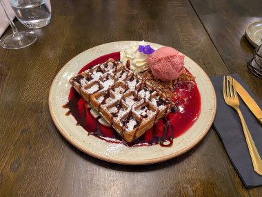 Çikolata soslu lezzetli waffle 'lar, pudra şekeri, krem şanti ve ahşap masada çilekli dondurma.