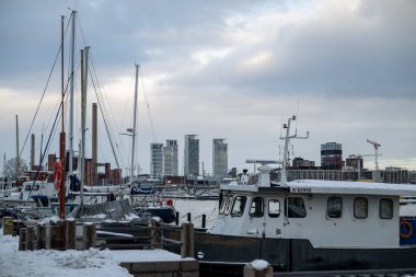 Helsinki, Finlandiya - 23 Kasım 2024: Karla kaplı liman, arka planda bulutlu bir gökyüzünün altında tekne, direk ve şehir silueti yer alıyor