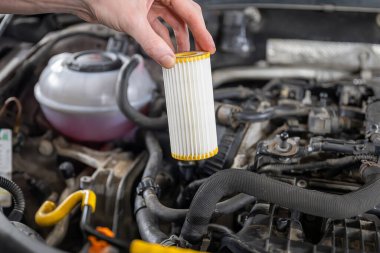 Hand holding a clean oil filter over a car engine in a maintenance setting, showcasing automotive care and repair tools clipart