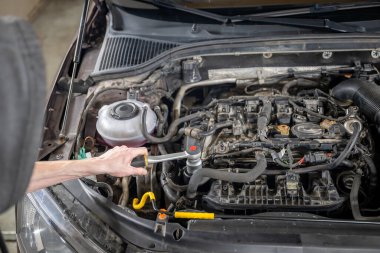 Mechanic examining car engine with hood open, wearing gloves, indoors in a garage. Concept of vehicle repair and maintenance clipart