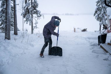 Kar küreği kullanarak karlı arka planda kar temizleyen bir adam. Kış görevi kavramı