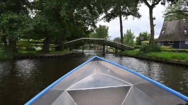 Hollanda, Giethoorn 'da yemyeşil ağaçlar ve çimlerle çevrili dar bir kanalda yüzen metal tekne.