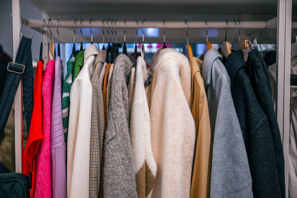 Разнообразная красочная и стильная одежда, висящая на металлической полке в шкафу. Уютная и модная одежда в различных текстурах и стилях