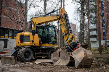Sarı tekerlekli kazıcı ve bir şehir şantiyesinde hidrolik yakalama eklentisi var.